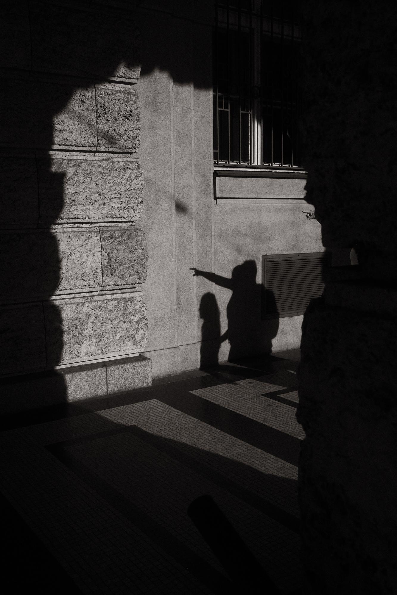 Siluety dvoch ľudí v tieni na ulici, jedna postava ukazuje rukou.