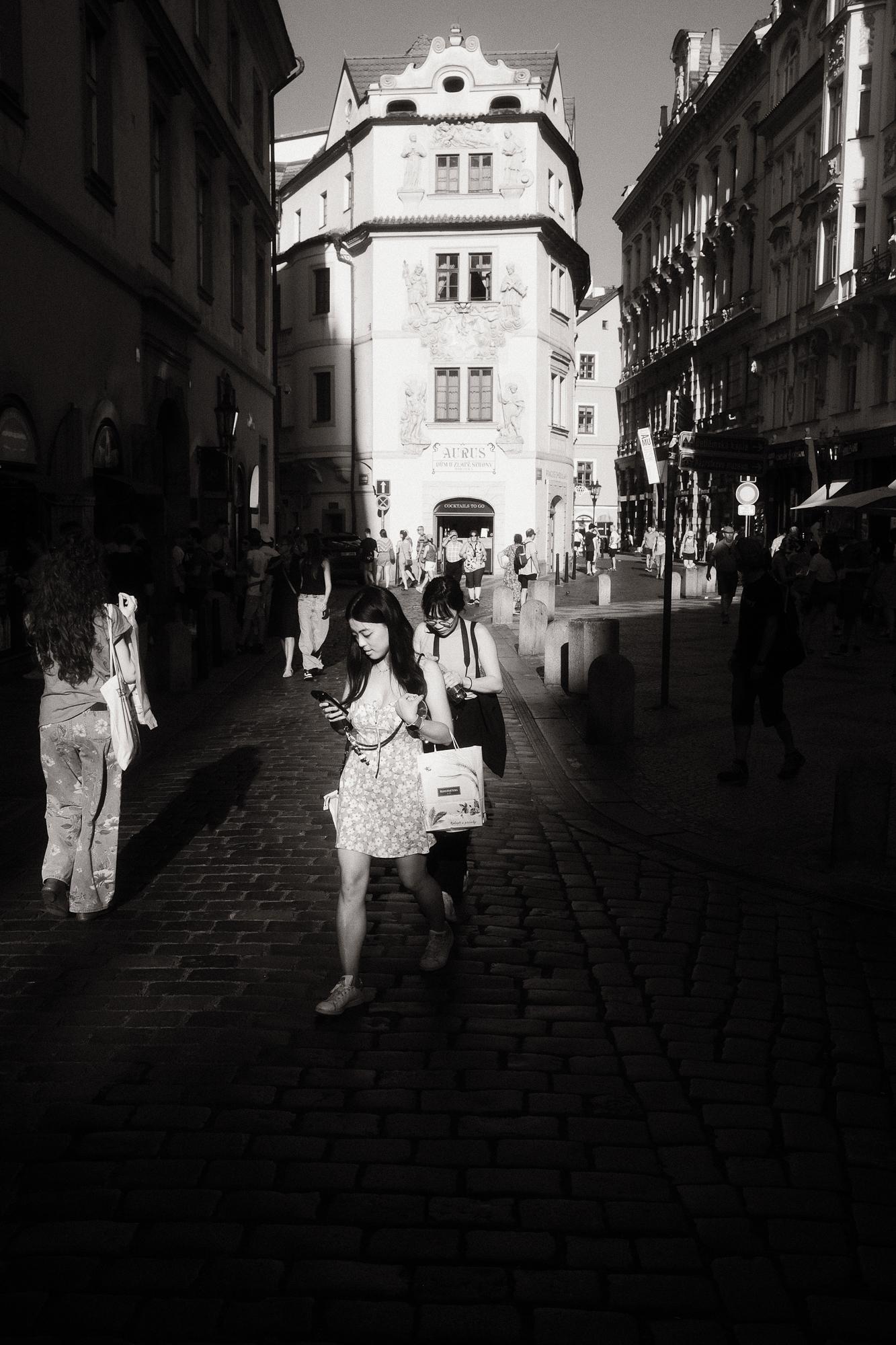 Čierno-biela fotografia rušnej mestskej ulice osvetlenej popoludňajším slnkom.