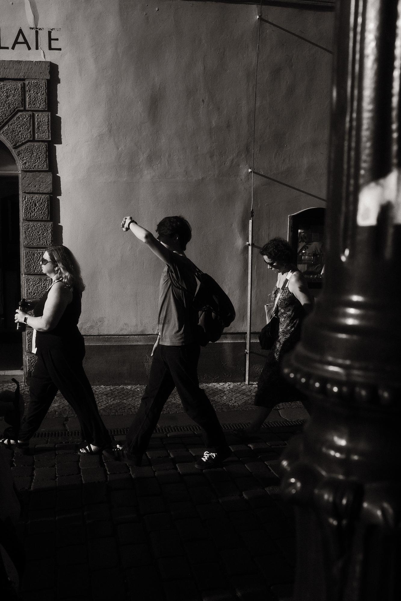 Čiernobiela fotografia ľudí kráčajúcich po ulici smerom do zapadajúceho slnečného svetla.