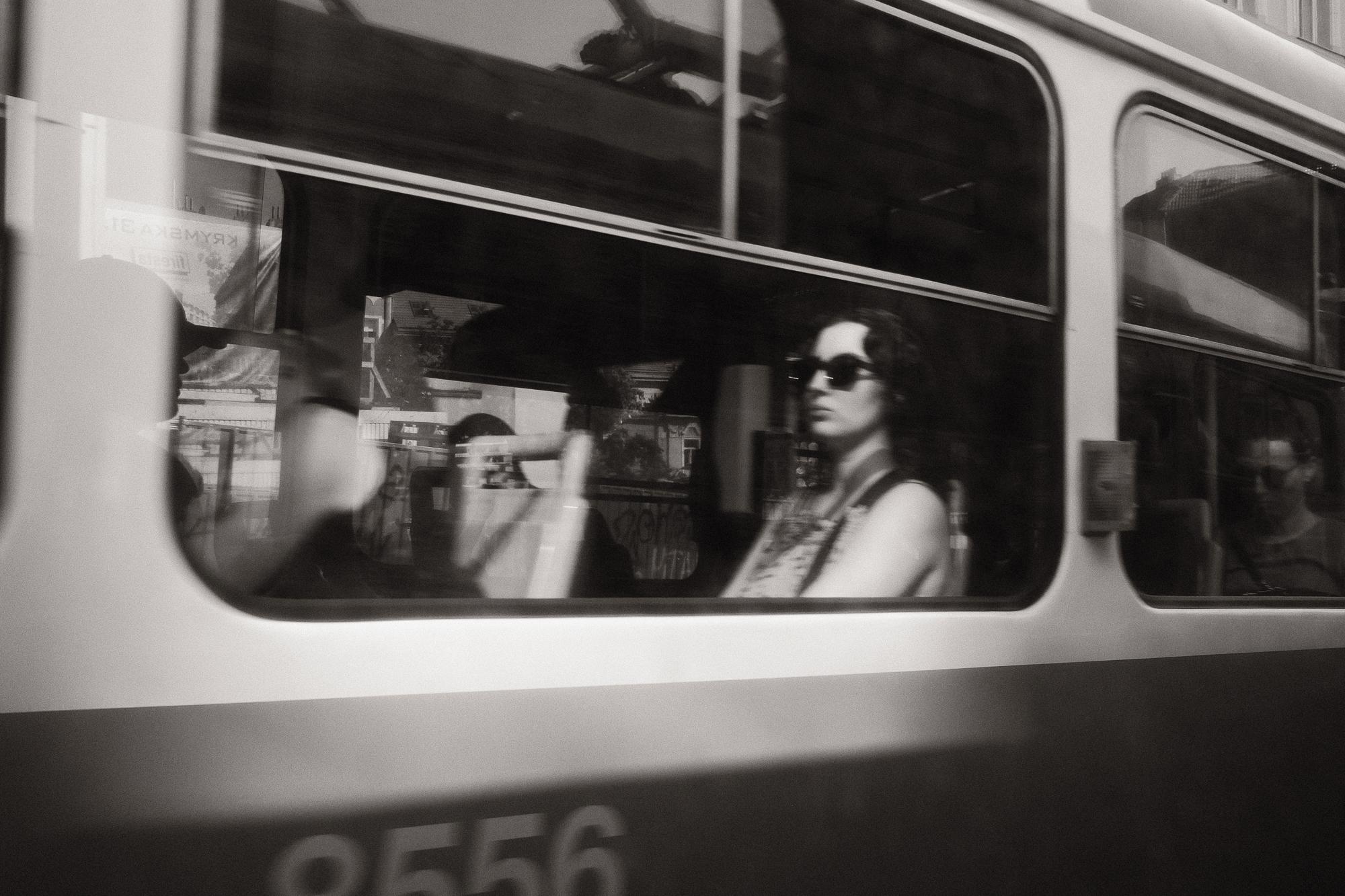 Čiernobiela fotografia ženy v slnečných okuliaroch sediacej v električke.