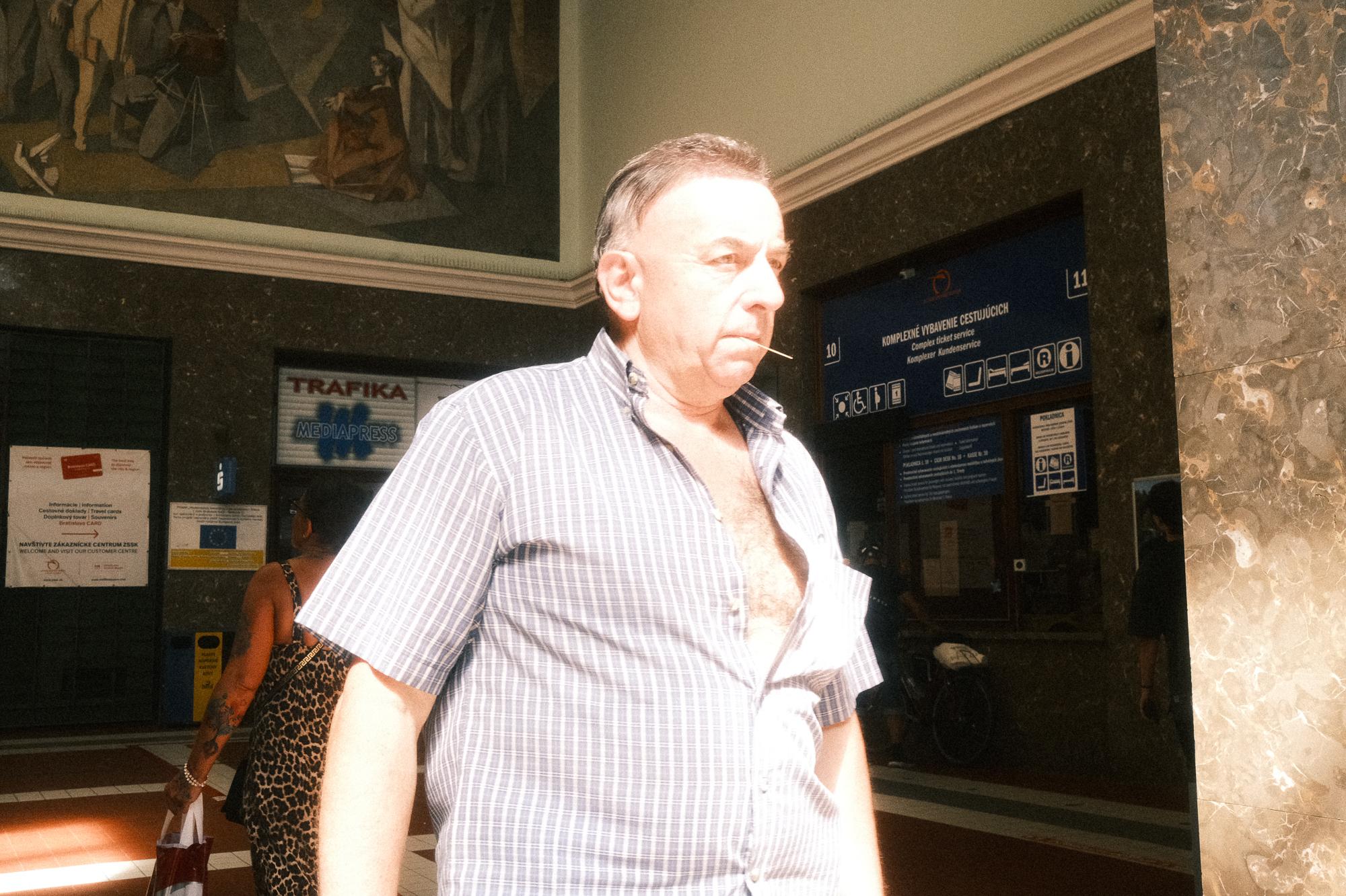Muž v prúžkovanej košeli kráča po slnkom zaliatej haly hlavnej stanice v Bratislave.