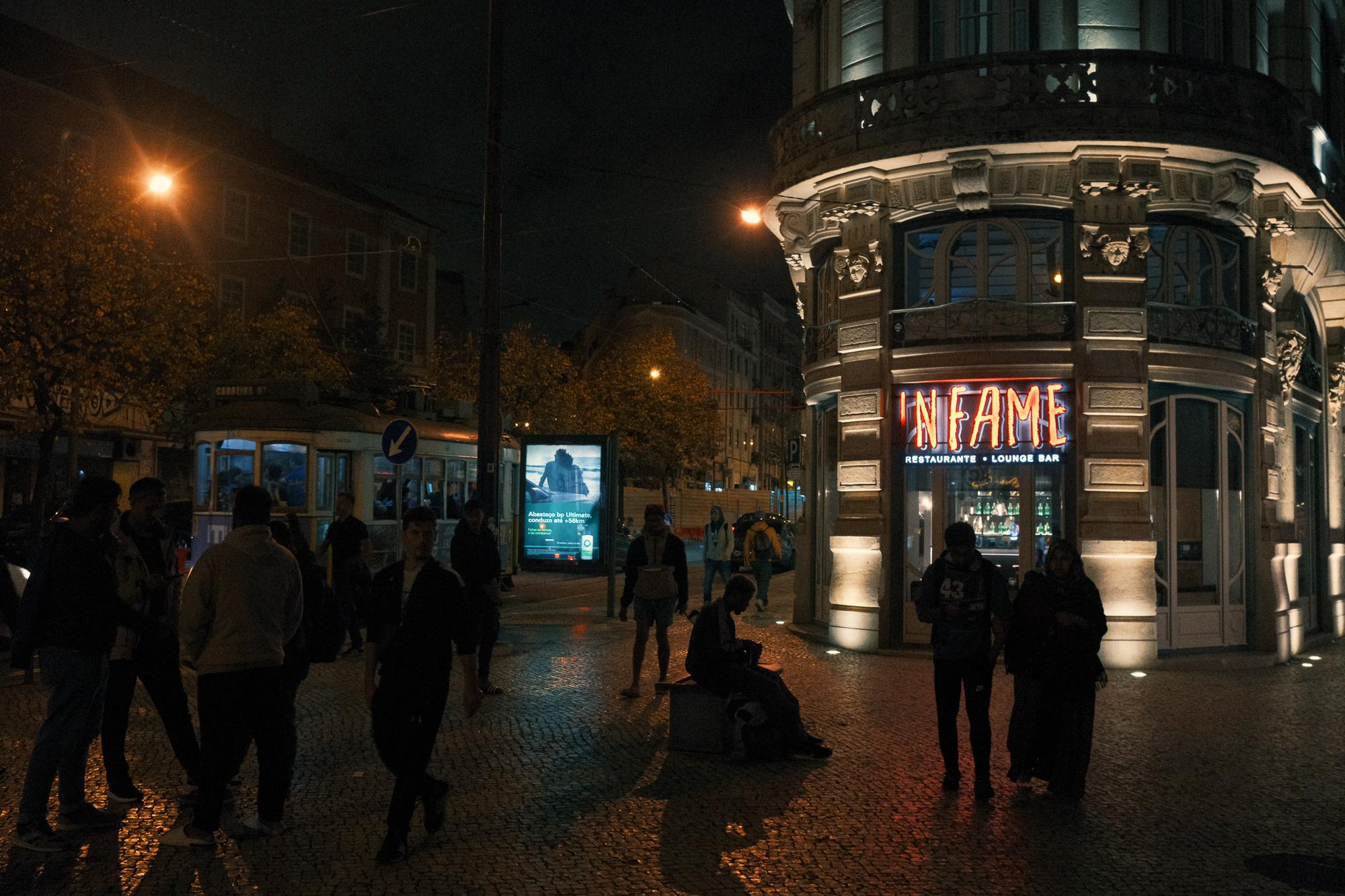 Nočná ulica osvetlená lampami a výkladom reštaurácie.