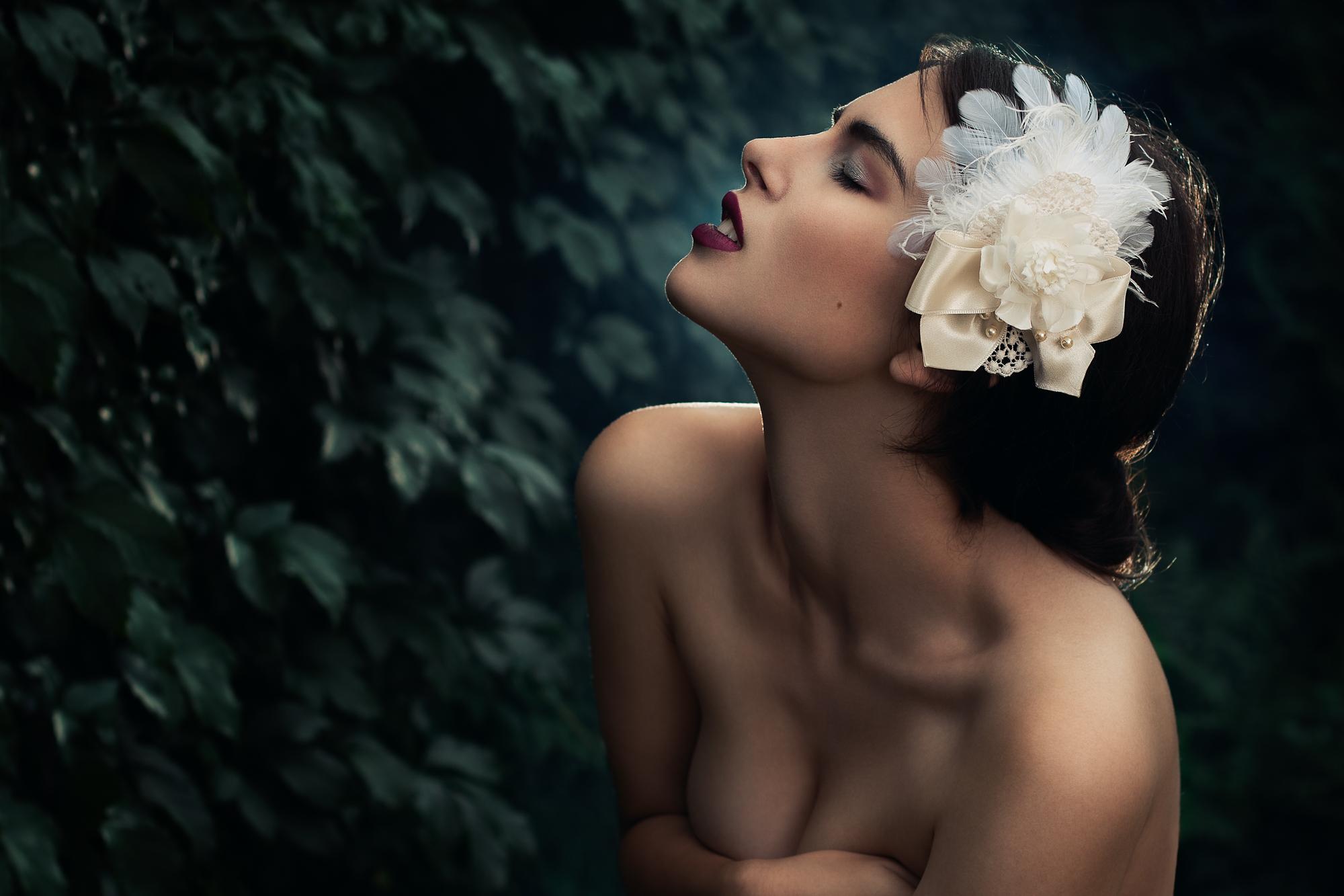 Emotívny portrét ženy o zatvorenými očami s veľkou ozdobou vo vlasoch pred tmavo zeleným brečtanom.