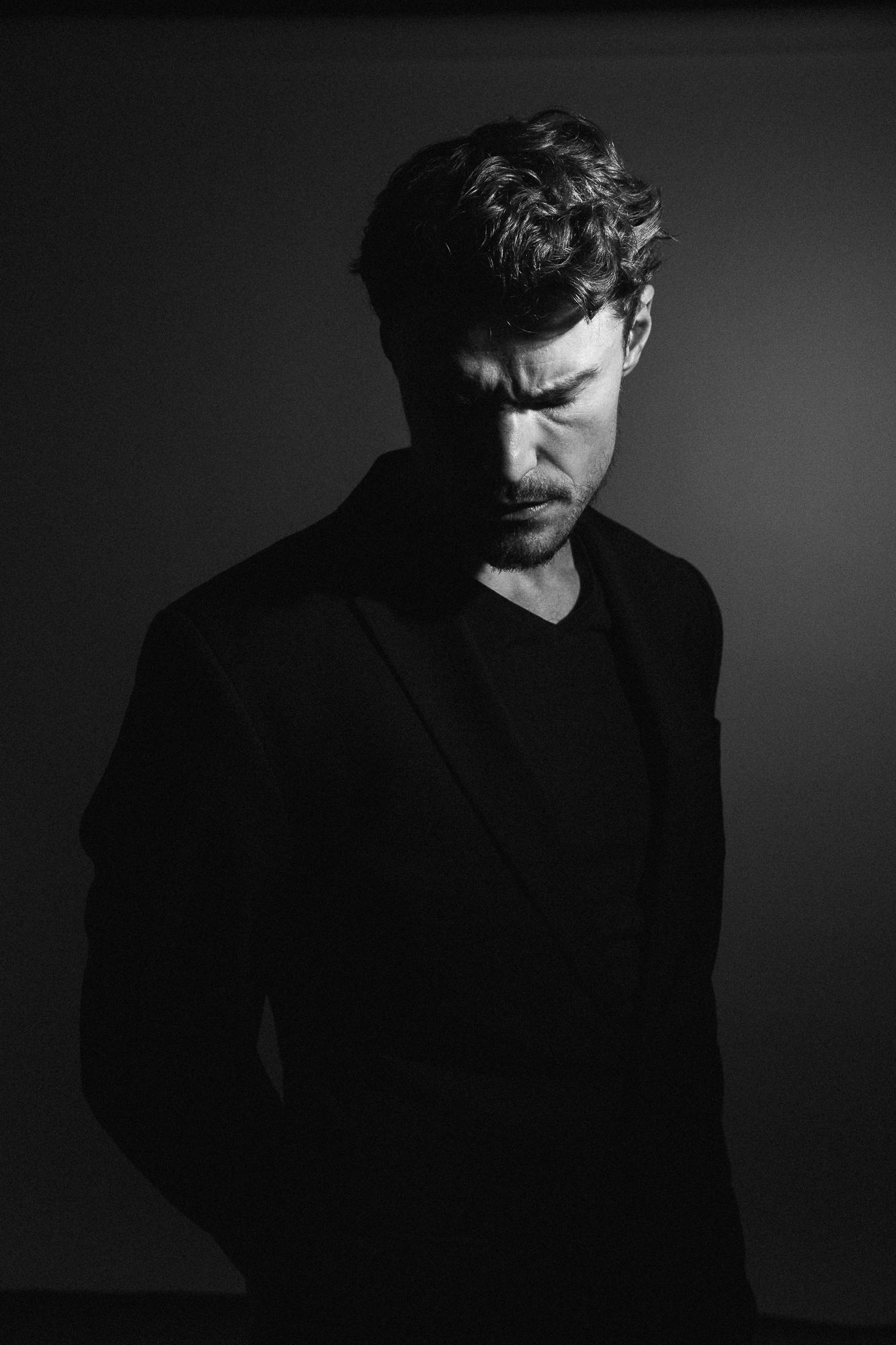 Čiernobiela fotografia muža v tmavom obleku, ktorý má zamyslený výraz a je osvetlený z boku. V atliéri v Pezinku.