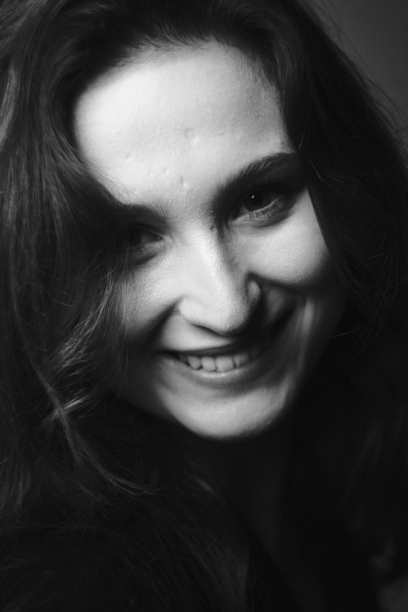 Čiernobiely portrét usmievajúcej sa ženy s voľnými vlasmi, zameraný na krásny úsmev a oči.