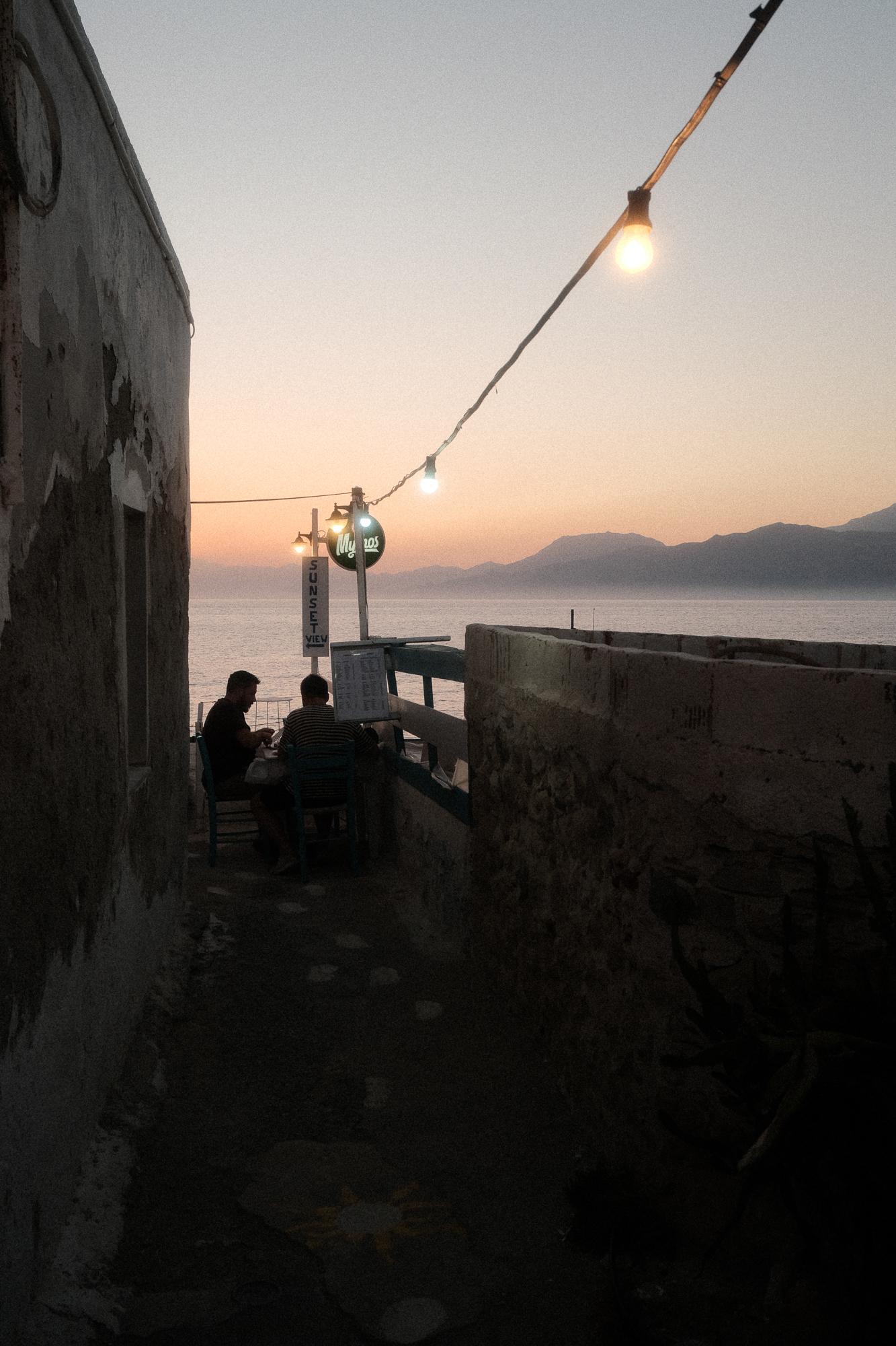 Úzka ulička vedúca k malému bistru, pri západe slnka v mestečku Matala, Grécko.