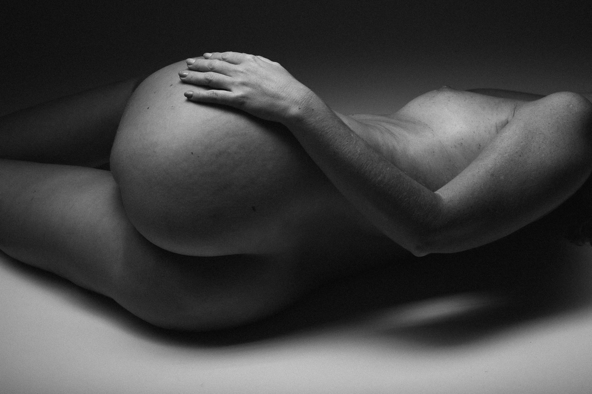 Black and white artistic nude photograph capturing an intimate pose of the female body, emphasizing the gentle curves and texture of the skin. Studio Pezinok.