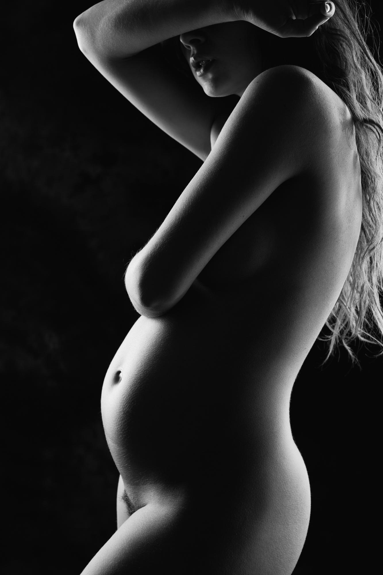 Black and white artistic nude photograph showing a silhouette of pregnant woman with soft lighting, emphasizing the body's curves. Bratislava.