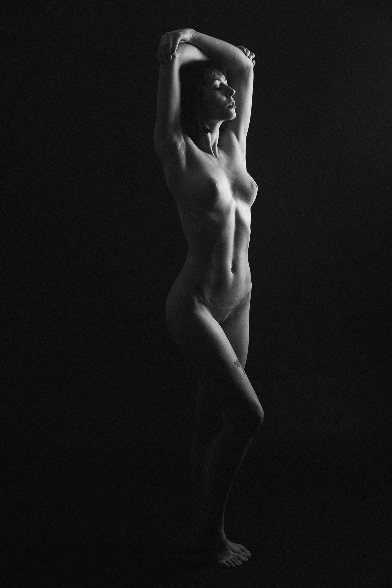 Black and white artistic nude photograph with soft shadows highlighting the female form, captured at Studio Pezinok.