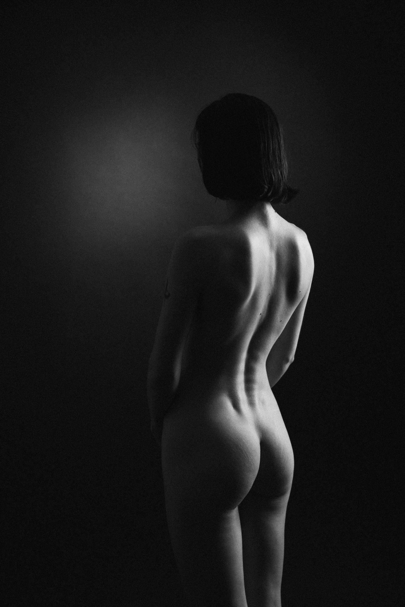 Black and white artistic nude photograph showing a female figure from behind with a focus on the elegant curves of the back and the bottom. Studio Pezinok.
