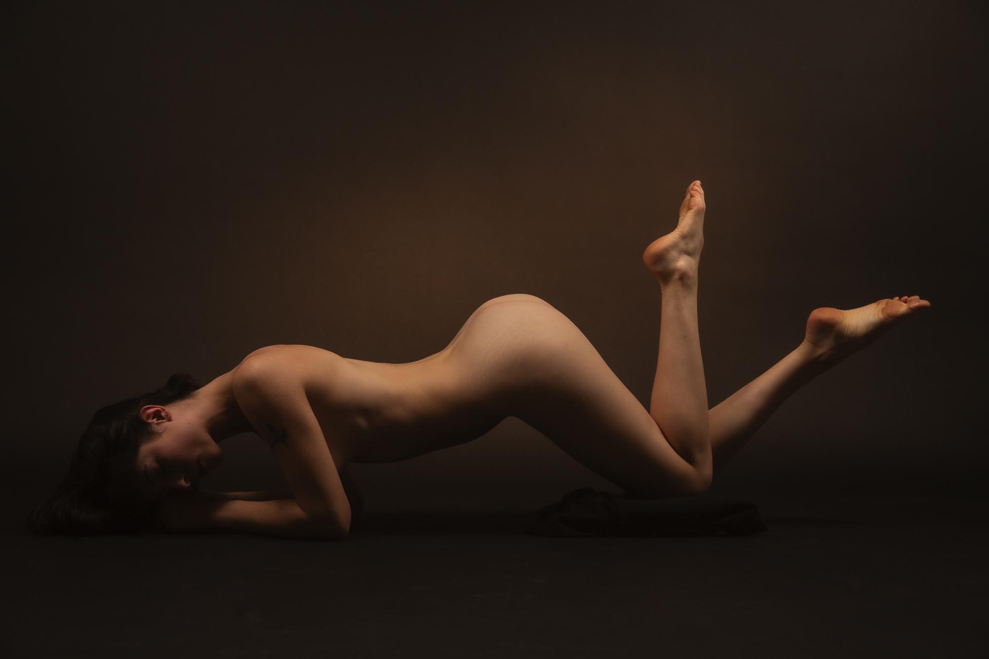 Artistic nude photograph capturing a female figure in a dynamic pose in soft lighting. Studio Pezinok.