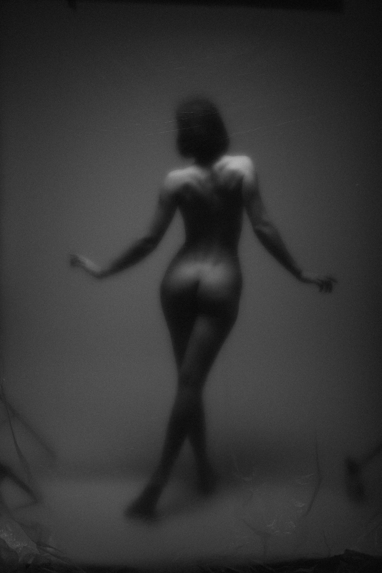 Čierno-biely umelecký akt zachytávajúci elegantnú ženskú siluetu v jemnom osvietení, vytvára hmlistý a éterický efekt. Fotografia z Ateliér Pezinok.