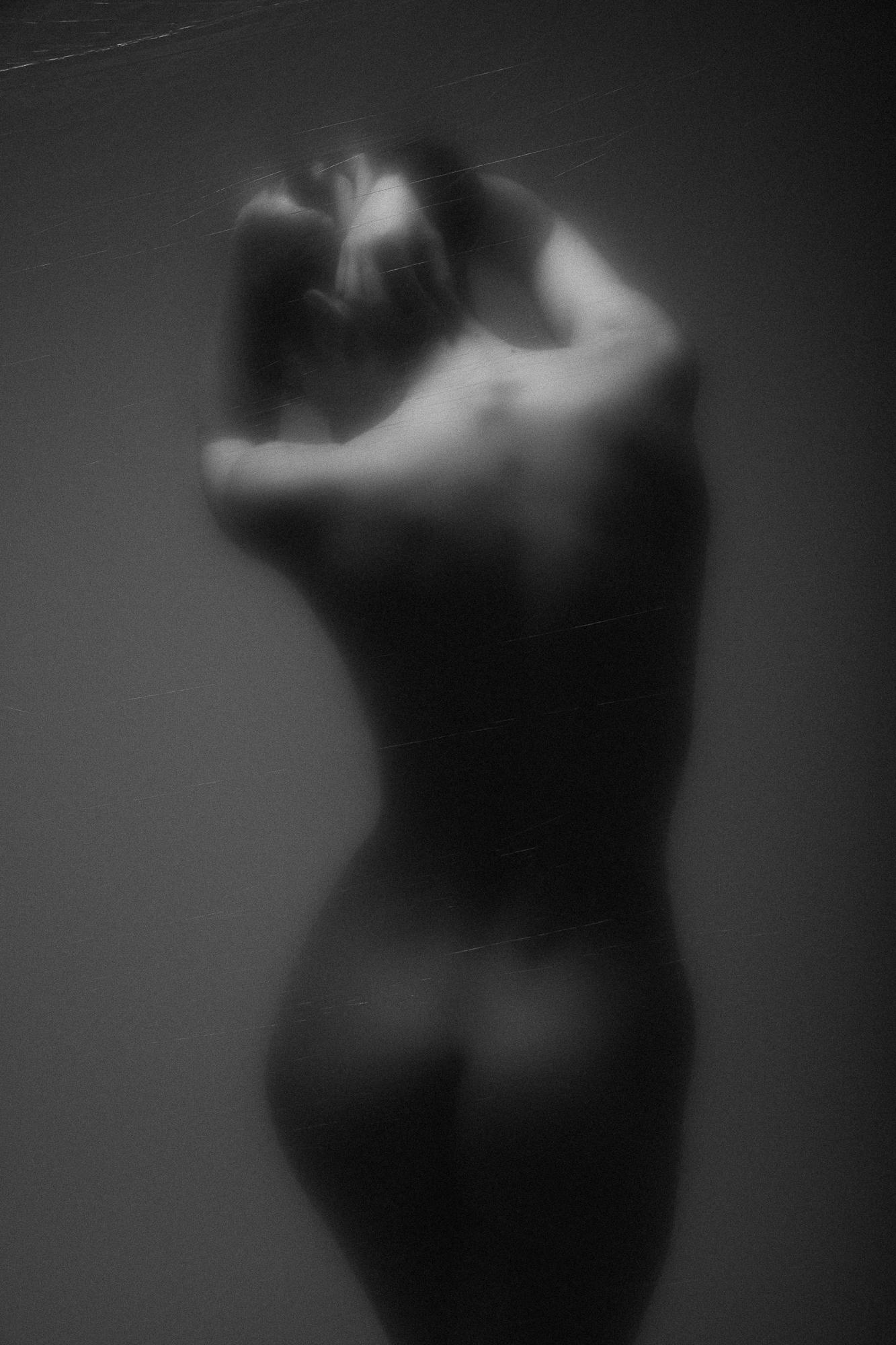 Black and white artistic nude photograph depicting a female figure with a subtle play of light and shadows, enhancing the natural lines of the body. The photo was taken in Studio Pezinok.