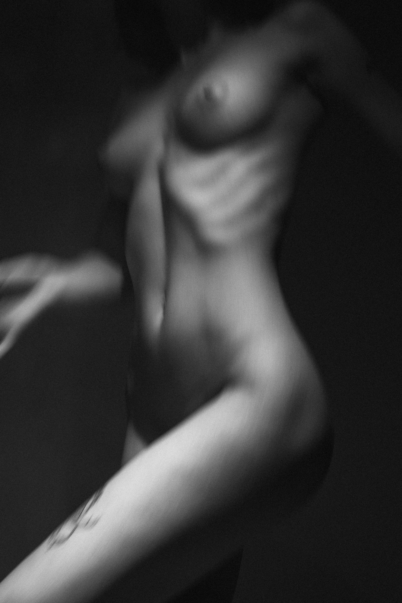 Black and white artistic nude photograph with soft lighting highlighting the body's curves in a dynamic pose. Studio Pezinok.
