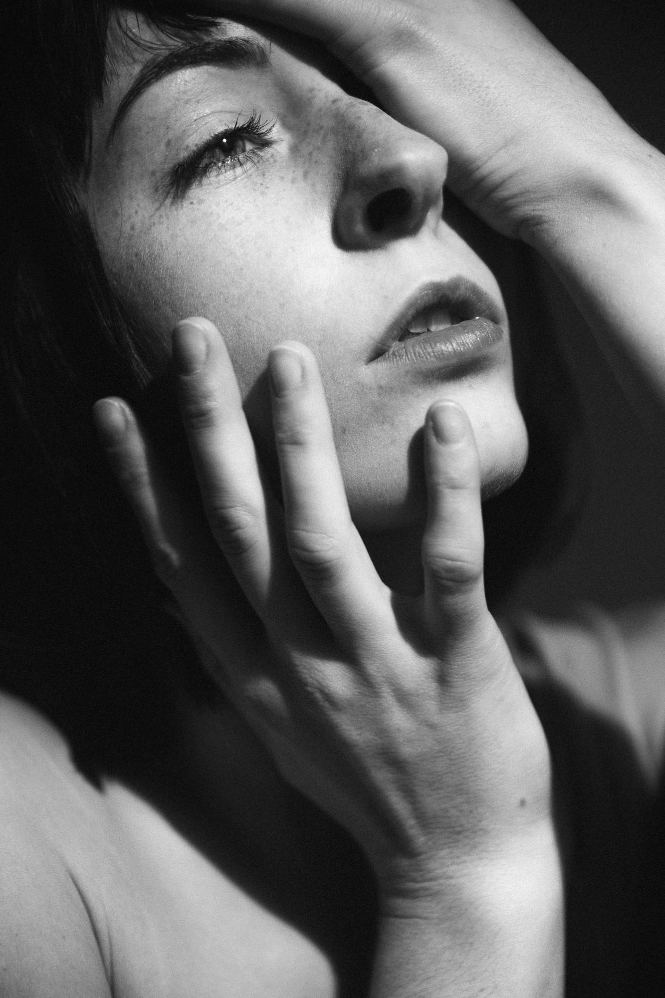 Čierno-biely portrét ženy s rukami položenými na tvári, so zamysleným emotívnym výrazom.