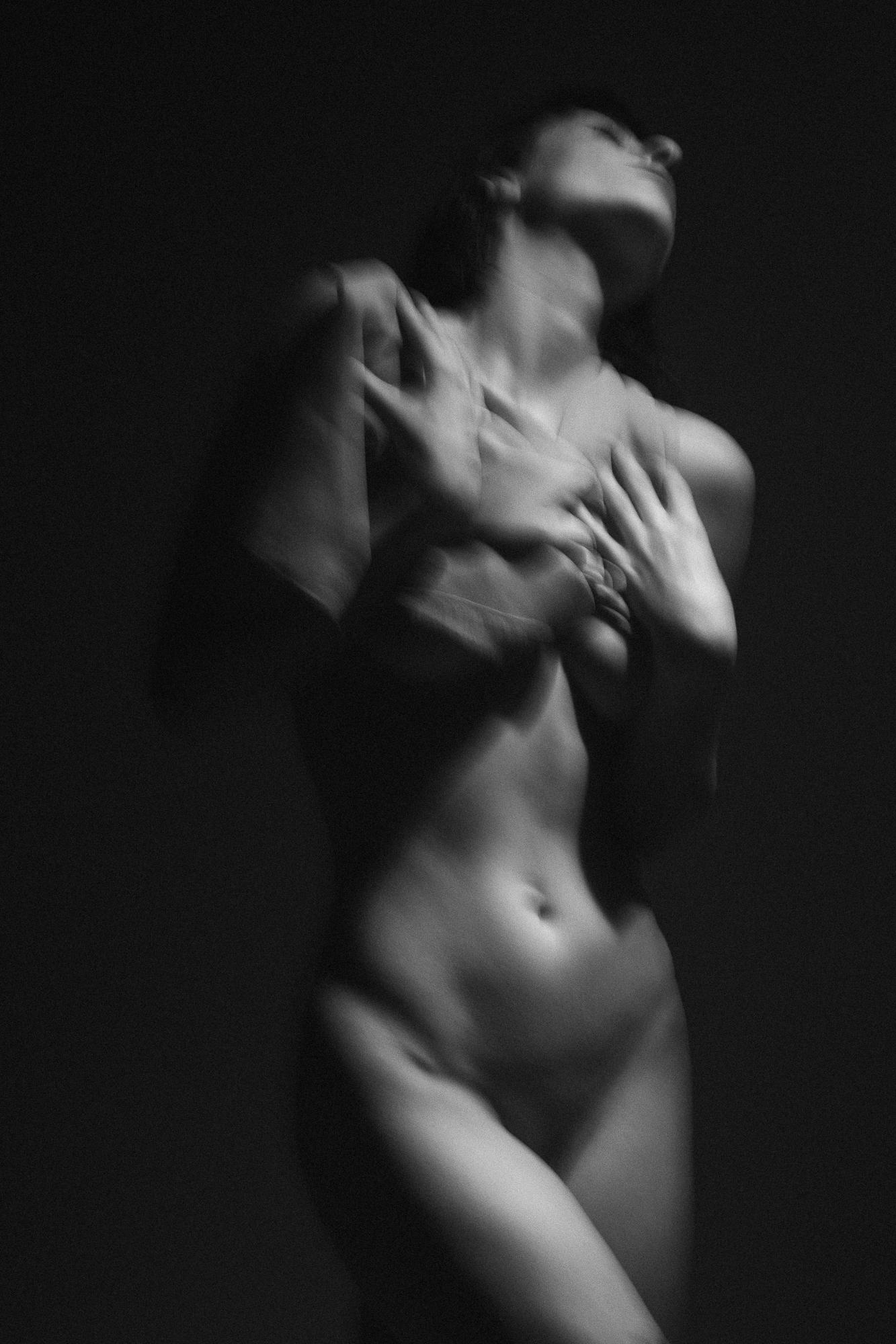 Slightly blurred black and white artistic nude photograph of a woman in motion with soft lighting and contrast of shadows. Studio Pezinok.