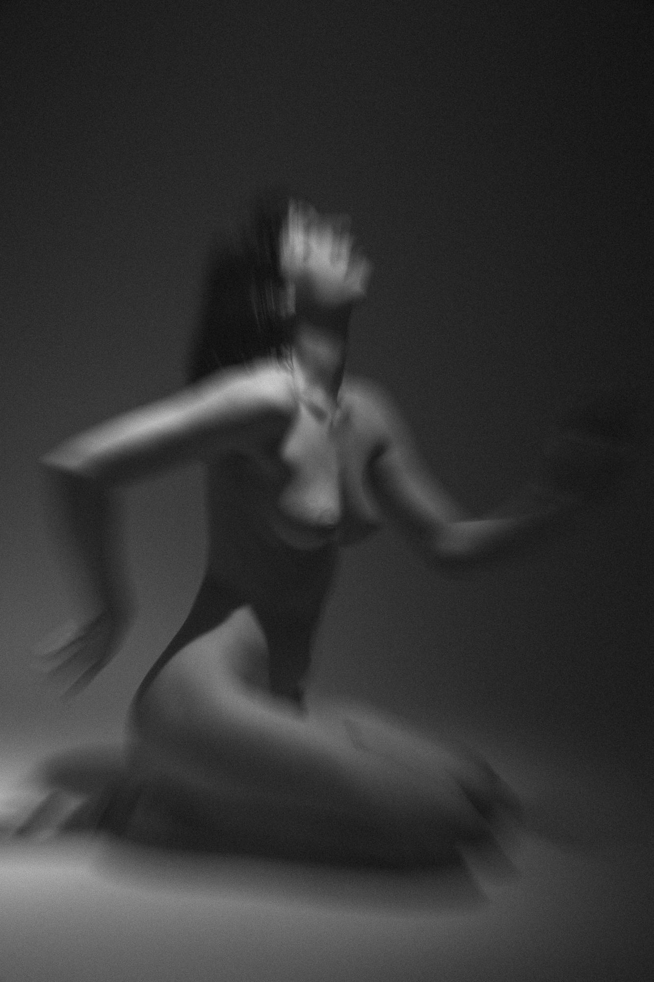 Black and white artistic nude photograph featuring soft lines and a blurred silhouette of a woman in motion. Studio Pezinok.