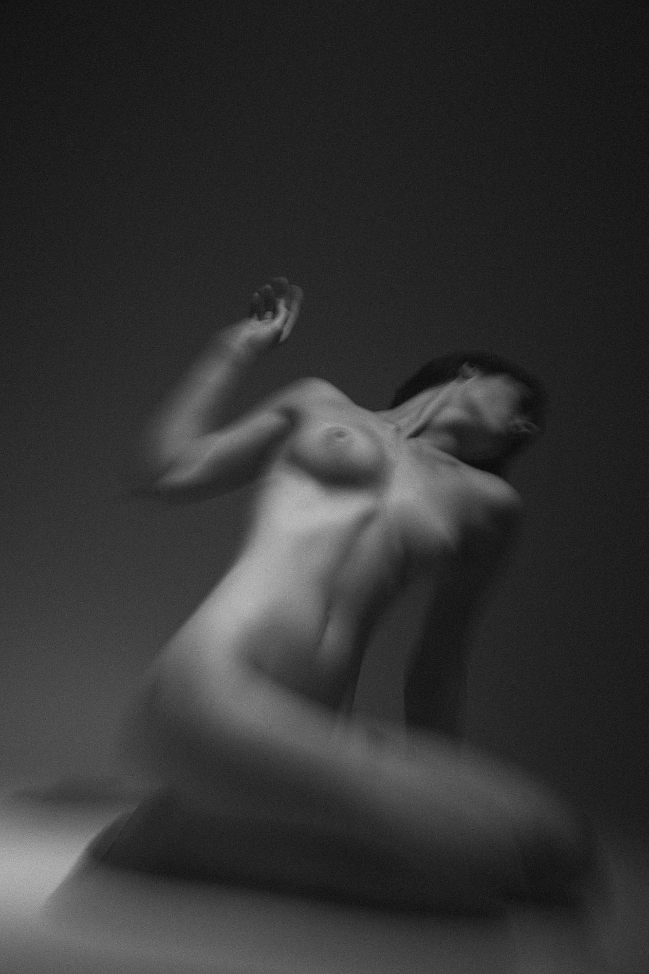Black and white artistic nude photograph capturing the delicate curves of a sensuously posed female figure against a dark background. Studio Pezinok.